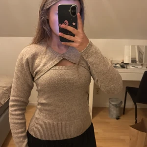 Beige stickat sett bolero+tubtopp - Säljer en beige stickad bolero+tubtopp över bröstet. Tröjan har lång ärm, ribbade muddar och en snygg, figurnära passform. Perfekt för dig som vill ha något trendigt och annorlunda i garderoben. Koftan är S och toppen i M. Nypris för båda 450kr. 