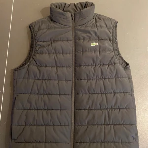 Lacoste väst  - Aldrig använd. Lappen finns kvar som lös, vilket visas på bilden. Västen har två sidfickor och en innerficka. Västen har också en inbyggd luva i kragen som kan tas fram. Vänligen kontakta vid frågor eller vid bud :) 