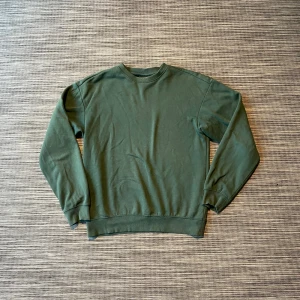 Grön sweatshirt från H&M  - En enkel och chill grön sweatshirt från H&M i relaxed fit. Tröjan har rund hals, långa ärmar och ribbade muddar vid ärmslut och nederkant. Perfekt för dig som gillar en clean look och vill ha något bekvämt till vardags.