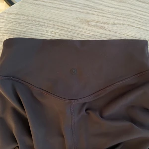 Bruna leggings från Lululemon - Mörkbruna leggings från Lululemon med hög midja och tight passform. Tillverkade i ett mjukt och stretchigt syntetmaterial som sitter skönt mot kroppen. Perfekta för träning eller chill dagar.