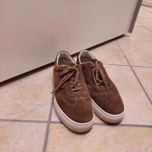 Bruna mockasneakers från Vagabond - Snygga bruna sneakers från Vagabond i mocka med vita, platta sulor och klassisk snörning. Skorna har en stilren och enkel design som passar till det mesta. Perfekta för dig som gillar en clean och avslappnad look.