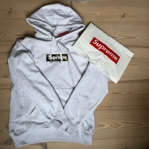 Supreme box  hoodie med camo logo - Supreme hoodie i ljusgrått med snörning. På bröstet finns en  Supreme logga med camouflage mönster. 10/10 skick.