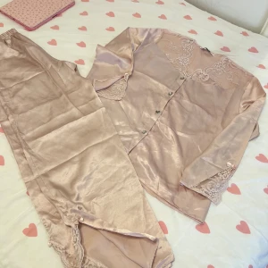 Lyxig satin rosa pyjamas - Lyxig satin pyjamas i puderrosa med fina spets slits i ärmen och fotleden. Helt ny, knappast använd. Liten i storleken , passar nog xs-m.