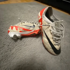 Nike Air Zoom fotbollsskor vit/röd - Säljer ett par Nike Air Zoom fotbollsskor i vitt med röda och svarta detaljer. Skorna har snörning, platt sula med dobbar och en sportig design. Perfekta för dig som vill sticka ut på planen med snygg stil och grym komfort.