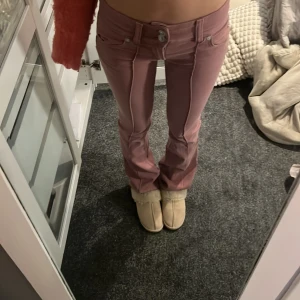 Lågmidjade jeans  - Säljer ett par snygga rosa jeans från Bershka i storlek 32. Byxorna har bootcut-snitt, låg midja och markerade sömmar framtill. Jag har sytt ner de till super lågmidajtt så de sitter väldigt lågmidjade 