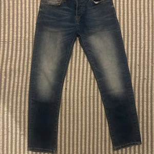 Blå slim fit jeans Premium Jeans - Snygga blå slim fit jeans från Premium Jeans, designade i Skandinavien. Jeansen har stretch för extra komfort och klassisk femficksdesign. Färgen är mellanblå med snygga slitningar och kontrastsömmar. Passar dig som gillar en smalare siluett och stilren look.