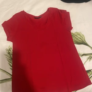 Röd v-ringad topp från KappAhl - Säljer en enkel och snygg röd topp från KappAhl i storlek S. Toppen har v-ringning, korta ärmar och är gjord i mjuk bomull. Perfekt för dig som gillar en klassisk och färgstark look. Passformen är normal och toppen är lätt att matcha med jeans eller kjol.