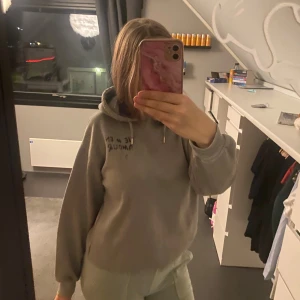 Grå hoodie med tryck och huva - Grå hoodie med texten 'JE M'EN AMOUR' och en stjärna tryckt på ryggen. Tröjan har huva med snörning, ribbade muddar och lång ärm. Perfekt för chill dagar och har en loose passform som ger en avslappnad vibe.