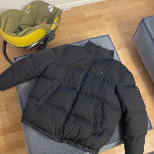 Svart pufferjacka från Tommy Hilfiger - Svart pufferjacka från Tommy Hilfiger med hög krage utan luva haft 1 år size XL nyskick 