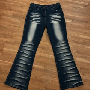 Blå bootcut jeans  - Bootcut jeans från Brooker i mörkblå tvätt med tydliga slitningar och ljusa partier framtill och baktill. Klassisk femficksmodell med dragkedja och knapp. Materialet är 96% bomull och 4% elastan för extra stretch och bekvämlighet.