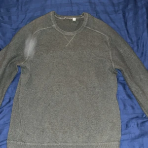 Grön stickad tröja med rund hals - En enkel och stilren grön stickad tröja med rund hals och ribbade muddar vid ärmslut och nederkant. Tröjan har långärmade raglanärmar och en diskret sömdetalj vid halsen. Perfekt för att hålla sig varm under kyliga dagar.