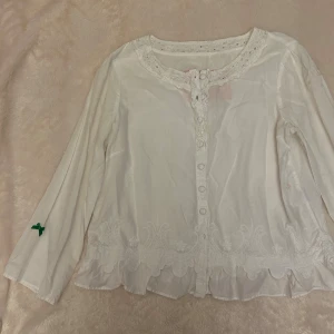Vit Odd Molly blus med spetsdetaljer - Supersöt vit blus från Odd Molly med broderade spetsdetaljer längs nederkant och halsringning. Långärmad modell med knappar framtill och romantiska volanger.💓💓 har en liten fläck på sidan, se bild 4. Uppskattar storlek M