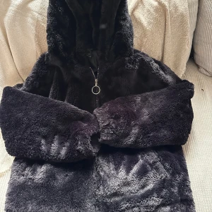 Svart päls bomberjacka från Factorie Audtralia - Mjuk och fluffig svart bomberjacka från Factorie Australia med huva och dragkedja framtill. Jackan har en oversized look, snörning i nederkant och är tillverkad i syntetiskt pälsmaterial. Perfekt för dig som vill ha en cozy vibe och sticka ut med en cool streetstyle.