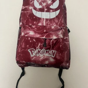 Pokémon ryggsäck med blixtmönster - Cool ryggsäck från Pokémon med mörkrött och vitt blixtmönster, stor tryckt Gengar-ansikte och Pokémon-logga på framsidan. Ryggsäcken har meshfickor på sidorna och justerbara svarta axelremmar. Perfekt för dig som gillar gaming och anime.