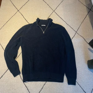 Marinblå stickad half zip-tröja - Säljer en marinblå stickad tröja från Zara med half zip och hög krage. Tröjan har ribbad struktur och långa ärmar, perfekt för kyliga dagar. Enkel och stilren design som funkar till det mesta.