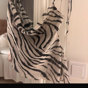 Zebramönstrad linnetopp med smala band - Säljer en snygg linnetopp med zebramönster i svart och beige. Toppen har smala axelband och en draperad halsringning som ger en cool och trendig look. Materialet är lätt och luftigt, perfekt för varma dagar eller när du vill sticka ut lite extra. Ger mig lite Bianca ingrosso ibiza vibe