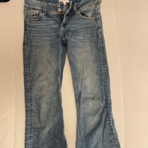 Blå bootcut jeans med fickdetaljer  - Snygga ljusblå jeans från Ginatricot med bootcut passform och klassisk femficksdesign. Jeansen har dubbla knappar och dragkedja i midjan samt bakfickor med lock och knapp. Materialet är mjukt denim med lätt tvättad look.