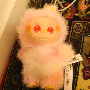 Lafufu/labubu - Söt och unik rosa plyschfigur från TheMonsiers med stora röda ögon och mjuk päls. Perfekt för samlare eller som present. Figuren är i mycket fint skick utan synligt slitage eller defekter. Märkestaggen sitter kvar. Är fejk. 
