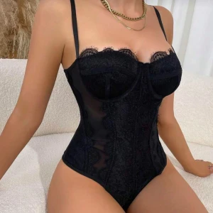 Svart spets body  - Supersnygg svart body med bygel och tunna axelband. Spetsdetaljer längs kanten och transparenta partier ger en lyxig och feminin vibe. Perfekt för dig som vill ha en unik och trendig look på fest eller vid middagar.