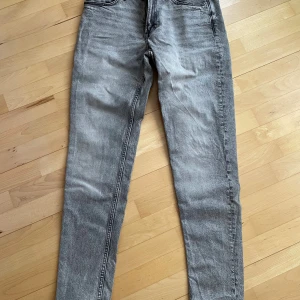 Grå tapered jeans skinny fit - Snygga grå jeans med tapered skinny fit och klassisk femficksdesign. Jeansen har en ljusgrå tvätt och raka sömmar, perfekta för en avslappnad men trendig look. Materialet är jeans och passformen är smalare vid benen.