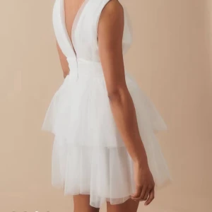 Vit tyllklänning med v-ringning - Supersöt vit kort klänning med flera lager tyll och bred midja. Klänningen har djup v-ringning både fram och bak, är ärmlös och har en voluminös kjol som ger en fluffig look. Perfekt för dig som vill sticka ut med en romantisk och trendig stil.