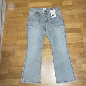 Grå bootcut jeans från Isay ordinarie pris runt 1050 - Snygga ljusgrå bootcut jeans från Isay med hög midja och klassiska fickor fram och bak. Jeansen har en cool tvättad look och är tillverkade i mjukt bomullsmaterial. Perfekt för dig som gillar retrovibbar och vill sticka ut med en trendig siluett.