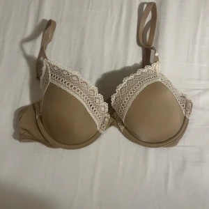 Aldrig använd Beige spetskantad bh från Calvin Klein storlek 70c - Snygg beige bh från Calvin Klein med vit spetskant upptill på kuporna. Storlek 70c. Aldrig använt den. Bh:n har släta kupor och justerbara axelband. Materialet är mjukt och stretchigt med en lyxig känsla. Perfekt för dig som gillar stilrena underkläder med en touch av spets.