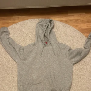 Grå hoodie från RYVLS med huva - Säljer en enkel och snygg grå hoodie från RYVLS i storlek 158/164. Tröjan har huva med snörning, ribbade muddar och en klassisk känguruficka framtill. Perfekt för chill dagar och passar till allt. Materialet är mjukt och känns skönt mot huden.
