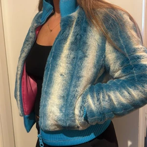 Blå-vit pälsjacka från Roxy - Säljer en unik pälsjacka från Roxy med blå och vita ränder, croppad passform och ribbade muddar. Jackan har dragkedja framtill och insidan är fodrad med rosa satin. Perfekt för dig som vill sticka ut med en färgstark look.