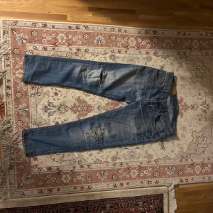 Blå skinny jeans från Dondup - Säljer ett par blå jeans från Dondup med skinny fit och slitna detaljer på benen. Jeansen har klassisk femficksdesign, ljus tvätt och snygga slitningar för en cool look. Passar dig som gillar smalare jeans med lite edge.