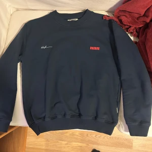 Mörkblå sweatshirt från Woodbird - Snygg mörkblå sweatshirt från Woodbird med tryck i rött och vitt både fram och bak. Tröjan har rund hals, ribbade muddar och är långärmad. Materialet är mjuk bomull som känns skönt mot huden. Perfekt för dig som gillar stilrena och coola prints.