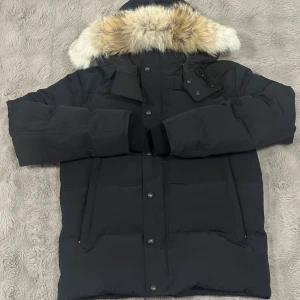 Svart dunjacka med päls från Canada Goose - Storlek S, bra skick köptes 2024. Päls ingår och dustbag.    Tror jag har kvitto kvar någonstans på mejlen🤝  whyndham black label                                                     Svart dunjacka från Canada Goose med stor huva och snygg pälsdetalj i beige och brun. Jackan har flera fickor med dragkedja och tryckknappar framtill. Perfekt för kalla vinterdagar och har en clean, modern look som funkar till allt.