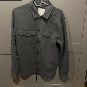Mörkgrå overshirt från Nifty - Riktigt snygg overshirt ifrån nifty i storlek 12 år. Passar runt 150-160 ungefär. Sitter normalt. Skönt material och vad jag vet säljs den inte längre.