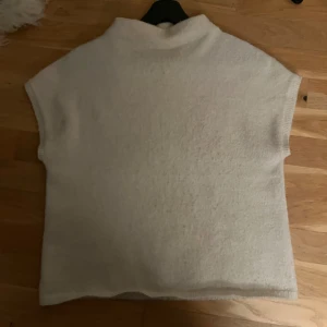 Beige stickad ärmlös tröja - Supermjuk och stilren beige stickad tröja med korta ärmar och hög krage. Perfekt att styla över en skjorta eller långärmad topp för en trendig lager-på-lager-look. Enkel och clean design som passar till många outfits.