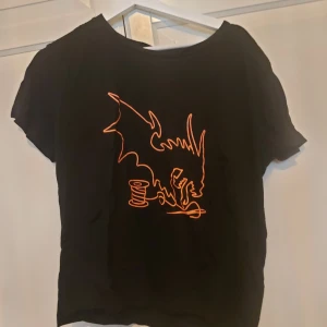 Svart t-shirt med orange draktryck - ⚠️ Skriv till mig innan köp!⚠️Svart närcon  t-shirt från 2025  i storlek M med ett coolt orange linjetryck av en drake och en trådrulle på framsidan. T-shirten har rund hals och korta ärmar, perfekt för dig som gillar unika motiv och vill sticka ut lite extra.