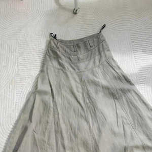 Beige långkjol med hög midja - Snygg beige långkjol med hög midja och bred linning. Kjolen har bälteshällor och markerade sömmar som ger en stilren look. Tillverkad i ett mjukt bomullstyg som känns skönt mot huden. Perfekt för dig som gillar en enkel och clean stil.