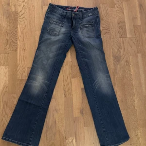 Blå bootcut jeans från Esprit - Snygga lågmidjade blå jeans från Esprit med bootcut passform och coola slitningar. Framtill finns dubbla fickor med dekorativa sömmar och baktill broderade fickor med Esprit-logga. Jeansen har klassisk knapp och dragkedja samt bälteshällor.