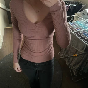 Ribbad rosa topp från NA-KD - Säljer en ribbad långärmad topp från NA-KD i en snygg rosa färg. Toppen har v-ringning med lätt rynkning vid bysten.