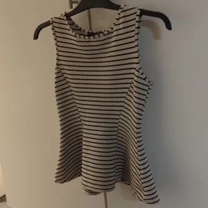 Randig top - Snygg top från Atmosphere i storlek 38. Topen är vit med svarta horisontella ränder och har en lätt utställd form. Den är ärmlös och har en rund halsringning. Materialet är ribbat och känns mjukt mot huden, perfekt för dig som gillar enkel och stilren design.