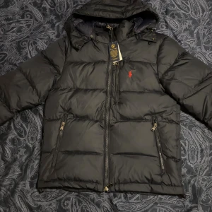 Polo Ralph Lauren herrjacka – storlek S, mörkblå - Stilren och varm dunjacka från Polo Ralph Lauren i mörkblå färg med klassisk röd logga på bröstet. Jackan är i mycket fint skick, knappt använd och med alla detaljer i toppskick. Perfekt till vintern – håller värmen utan att kännas tung.  🎁 Passar perfekt som julklapp, Black Friday-fynd eller bara en riktigt snygg vinterjacka till dig själv.  ✅ Storlek: S ✅ Färg: Mörkblå ✅ Skick: Mycket bra 