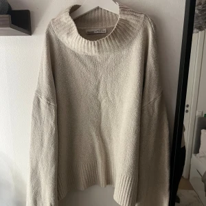 Beige polotröja från Pull&Bear - Säljer en beige polotröja från Pull&Bear i storlek M. Tröjan har en bred, ribbad krage och ribbade detaljer vid nederkant och ärmslut. Den är stickad och har en loose passform med långa ärmar, perfekt för att hålla sig varm under kyliga dagar.