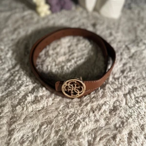 Brunt skärp från Guess - Säljer ett bälte från Guess för 170kr, Den är brun med guld detalj och är 110cm lång och är 2,3cm i bredd. Den har 10 hål för att ändra storlek på. 