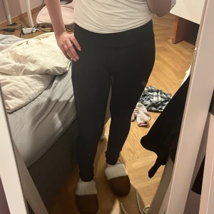 Svarta höga leggings med ficka - Säljer ett par svarta leggings med hög midja och praktisk ficka på sidan. De är tighta och stretchiga, perfekta för träning eller chill. Materialet är mjukt och följsamt, och de har en diskret logga bak. Snygga och enkla att matcha med allt.