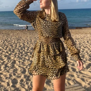 Leopardmönstrad kort klänning med volanger - Säljer en superfin kort klänning med leopardmönster och volanger. Klänningen har långa ärmar, markerad midja med smock och rund halsringning. Perfekt för dig som vill sticka ut med en trendig look. Materialet känns lätt och luftigt.