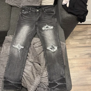 Svarta ripped jeans från Amiri - Snygga svarta jeans från Amiri med slitna detaljer och stora hål på knäna. Jeansen har en tvättad look, klassisk femficksmodell och smal passform. Perfekta för dig som gillar streetstyle och vill sticka ut med coola detaljer.