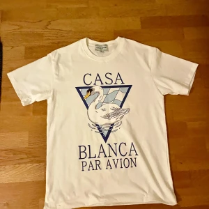 Vit t-shirt Casa Blanca med tryck - Vit t-shirt från Casa Blanca med stort grafiskt tryck på framsidan som visar en svan och texten 'Casa Blanca Par Avion'. Klassisk rund hals och korta ärmar. Materialet är mjuk bomull, perfekt för en chill och stilren look.