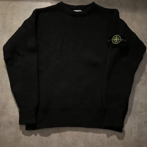 Svart stickad tröja från Stone Island - Svart stickad tröja från Stone Island med klassisk rund hals och ribbade muddar. Tröjan har den ikoniska Stone Island-loggan på vänster ärm. Perfekt för dig som gillar stilrena och tidlösa plagg med streetkänsla. Priset går att diskuteras💫