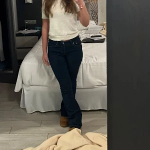 Mörkblå bootcut jeans - Säljer ett par mörkblå jeans med bootcut passform och hög midja. Jeansen har klassisk femficksdesign och är tillverkade i ett stretchigt denimtyg som sitter snyggt över höfterna och låren innan de släpper ut vid bensluten.