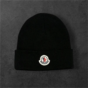  Moncler mössa  - Svart ribbstickad mössa från Moncler med klassisk uppvikt kant och broderad Moncler-logga framtill. Perfekt accessoar för kalla dagar och en stilren detalj till din outfit.