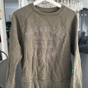 Olivgrön sweatshirt från Zadig & Voltaire - Snygg olivgrön sweatshirt från Zadig & Voltaire med broderad text framtill. Tröjan har rund hals, långa ärmar och är tillverkad i mjuk bomull. 